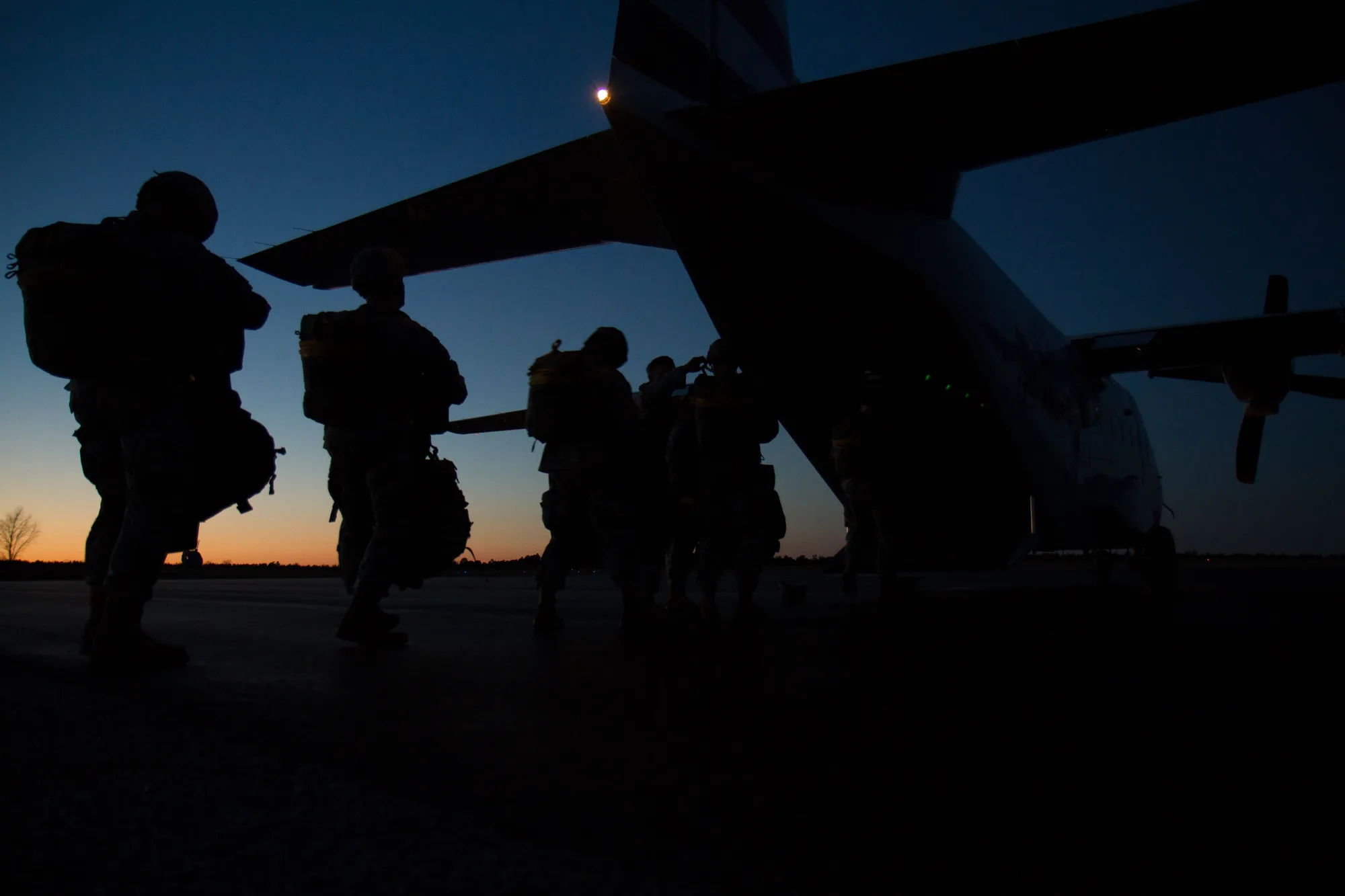 U.S. soldiers in full kit, silhouetted against the dusk sky, boarding an aircraft